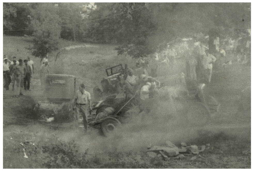 A black and white photograph of a jalopy race at the Perry Smith Farm. Pre-war vehicles kick up dust as they drive up an incline in a rural setting. Crowds of onlookers stand near the dirt track.