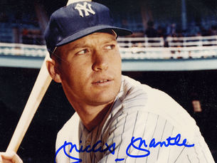 An autographed photo of Mickey Mantle standing on the mound at Yankee Stadium. Mantle is wearing a Yankees uniform and holding a bat. The photograph is signed with a blue marker.
