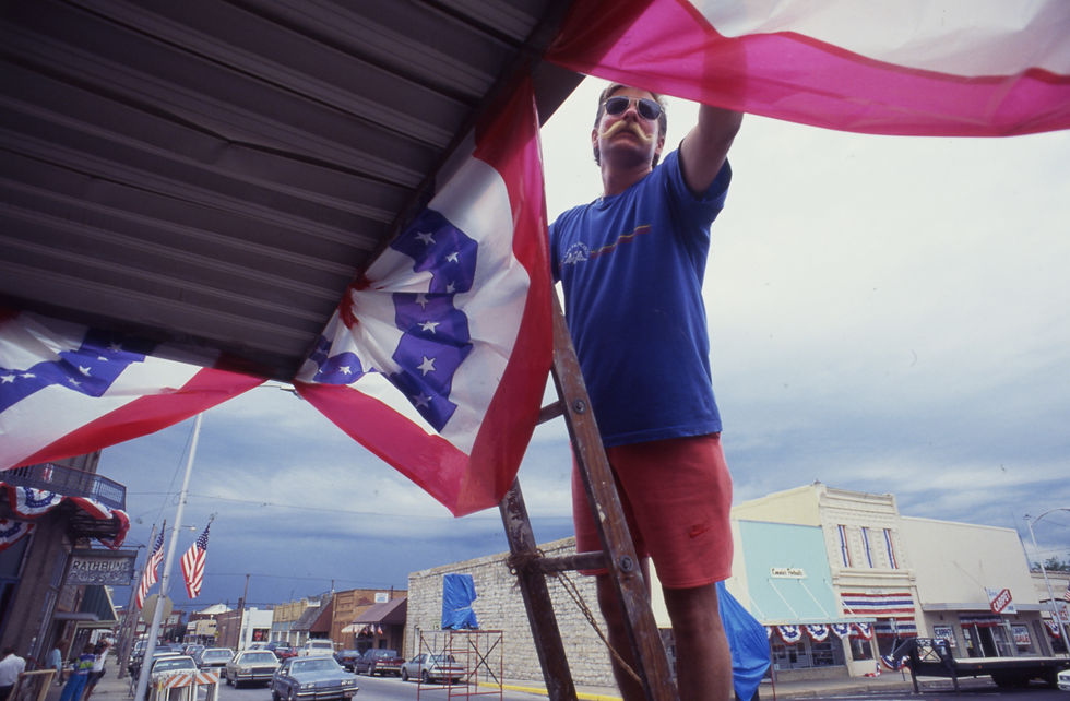 Jerry Minor stands on a ladder to adjust patriotic bunting in front of Ruth's Flowers on the Marshfield square.