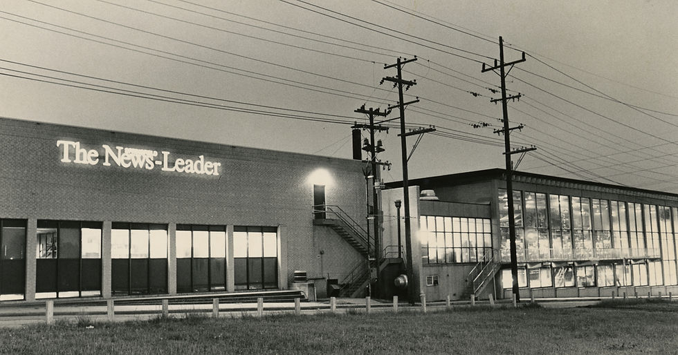 A black and white photo of the exterior of the Springfield News-Leader building on Boonville Avenue. A neon sign reading "The Springfield News-Leader" is on the facade. At right is the Leader's pressroom, visible through large windows.