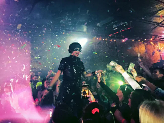 Crystal Methyd, a drag queen, performs in a black dress and bob wig at the Outland Ballroom. Confetti falls through the air and fans clamor to hand Methyd cash tips.