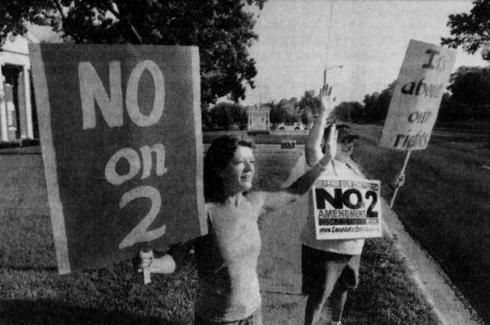 Kathy Wiley and Sherry Sappington stand on a sidewalk holdings signs expressing opposition to Amendment 2. Signs read: "No on 2" and "It's about our rights."
