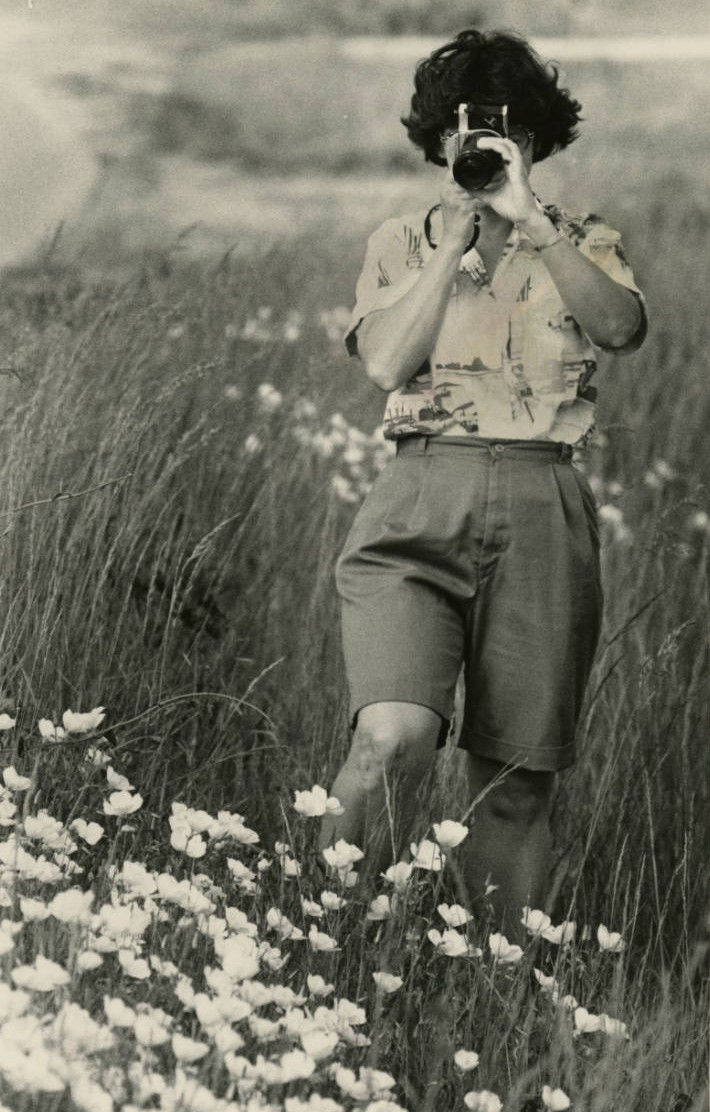 A black and white photograph of Mary Simmons photographing wildflowers.