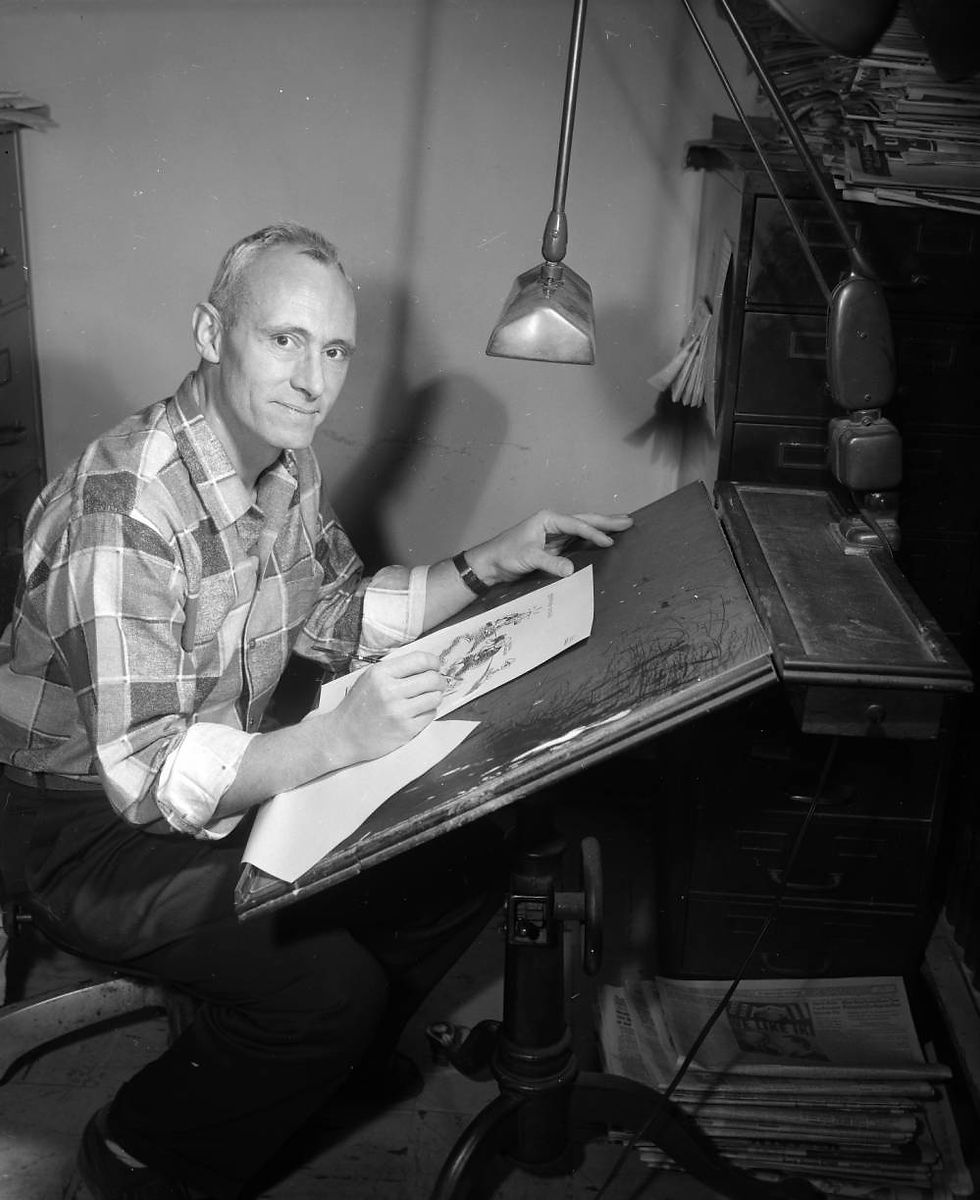 Bob Palmer works at a desk in a studio. Palmer is working on a cartoon.