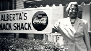 Alberta Ellis stands in front of her hotel. Text on sign is cut off, but what is visible reads: "Alberta's Snack Shack."