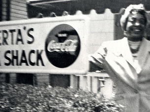 Alberta Ellis stands in front of her hotel. Text on sign is cut off, but what is visible reads: "Alberta's Snack Shack."