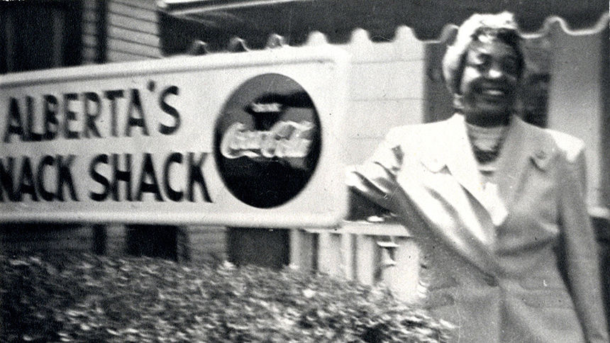 Alberta Ellis stands in front of her hotel. Text on sign is cut off, but what is visible reads: "Alberta's Snack Shack."