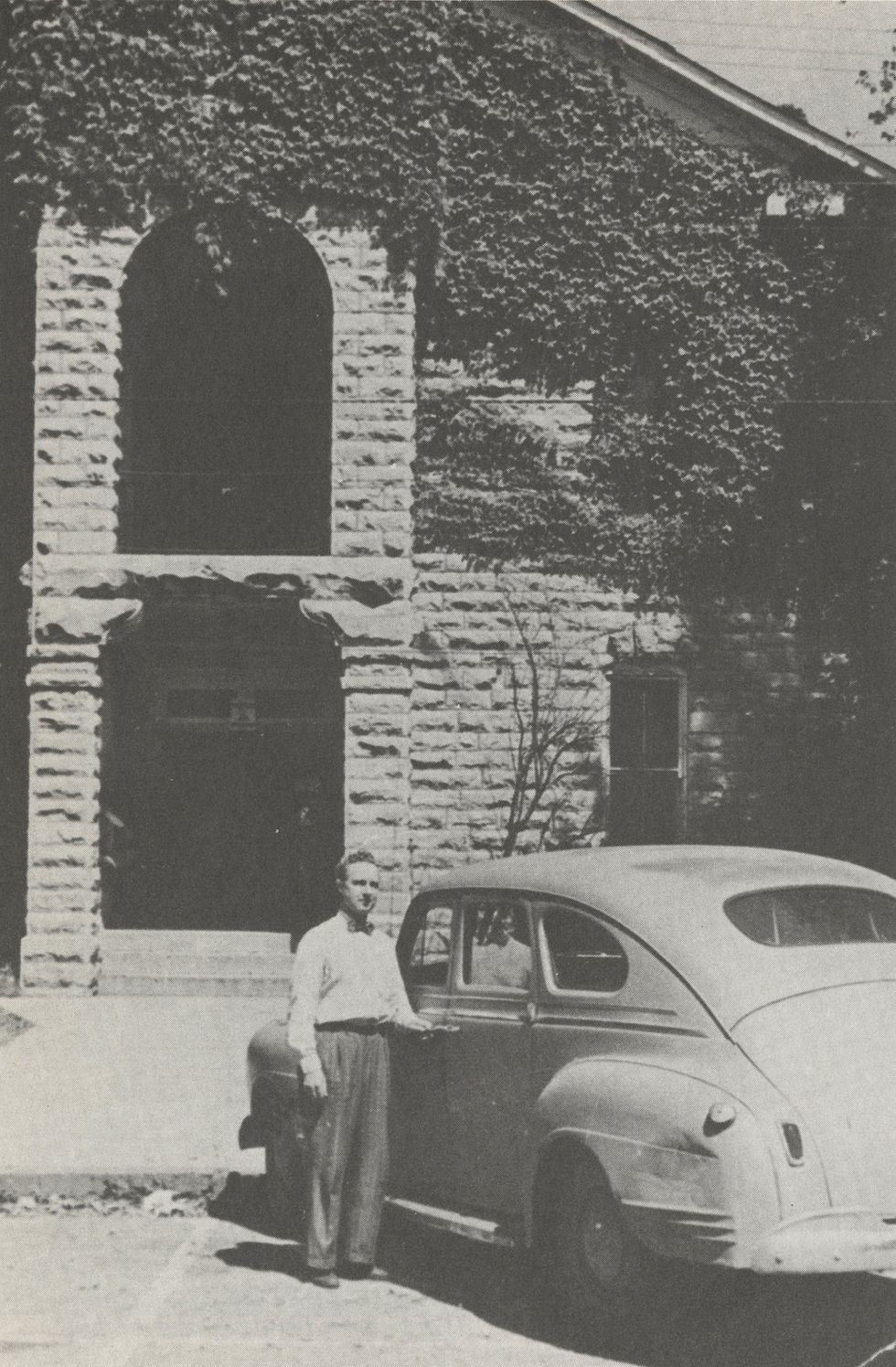 Douglas Mahnkey stands next to a car in front of the 1855 Taney County Courthouse in Old Forsyth. The front of the building is covered in ivy.