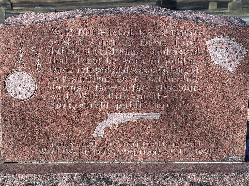 The back of Davis Tutt's headstone. The marker is a polished red granite. There are engraved images of a pocket watch, a revolver, and playing cards. Text on the headstone reads: "Wild Bill Hickok lost a family pocket watch to Davis Tutt during a card game, and asked that it not be worn in public. Davis refused and was challenged to a gunfight. Davis lost his life during a face to face shootout with Wild Bill on the Springfield public square. "