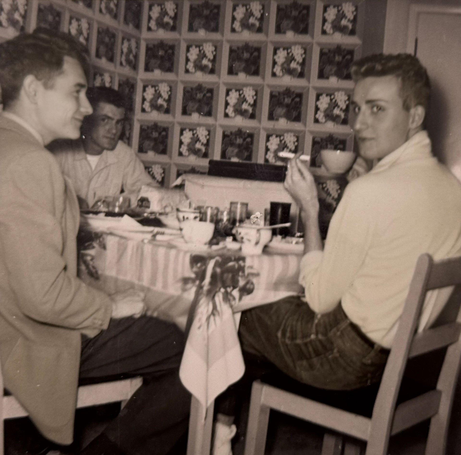 Three unidentified men sit around a table. One is smoking.