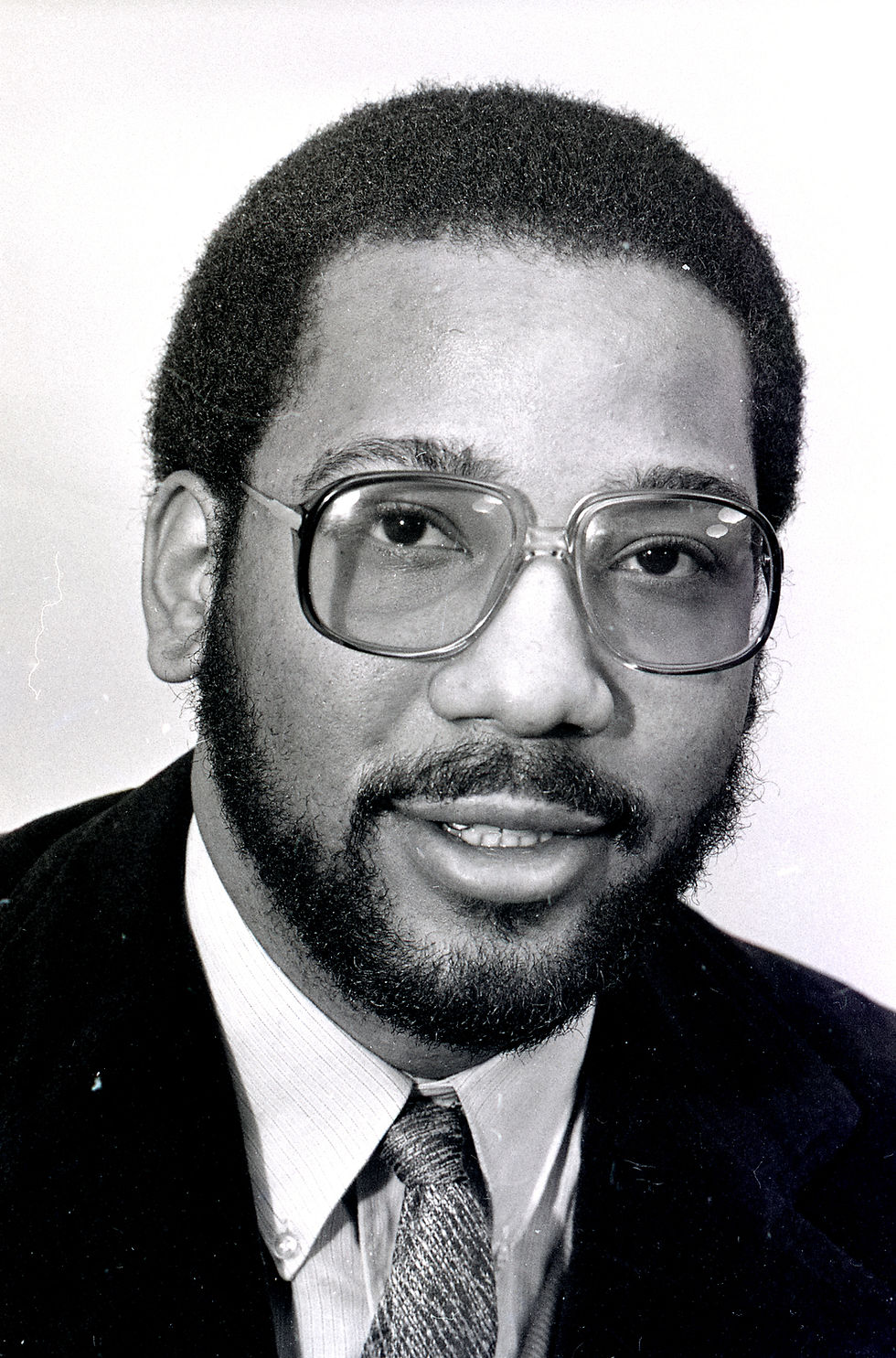 Portrait of Rory Calhoun, a young African American man wearing a suit, with short hair, mustache, and beard, and glasses.