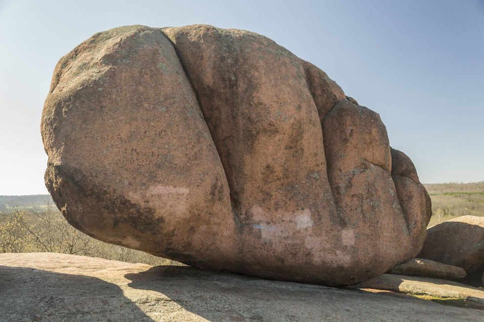 A granite boulder or "Elephant Rock" at Elephant Rocks State Park sits atop a larger outcropping of rock. The boulder is worn smooth by years of erosion and is subdivided by deep faults.