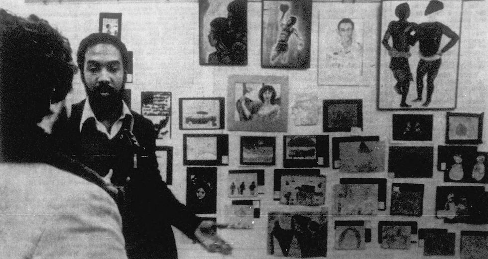 Artist Harold McPherson speaks with a reporter in front of a gallery of artwork by Black children.
