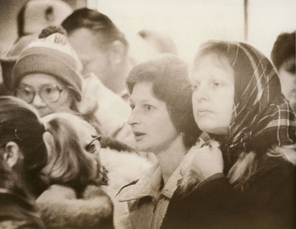 Men and women of various ages wait in line outdoors.