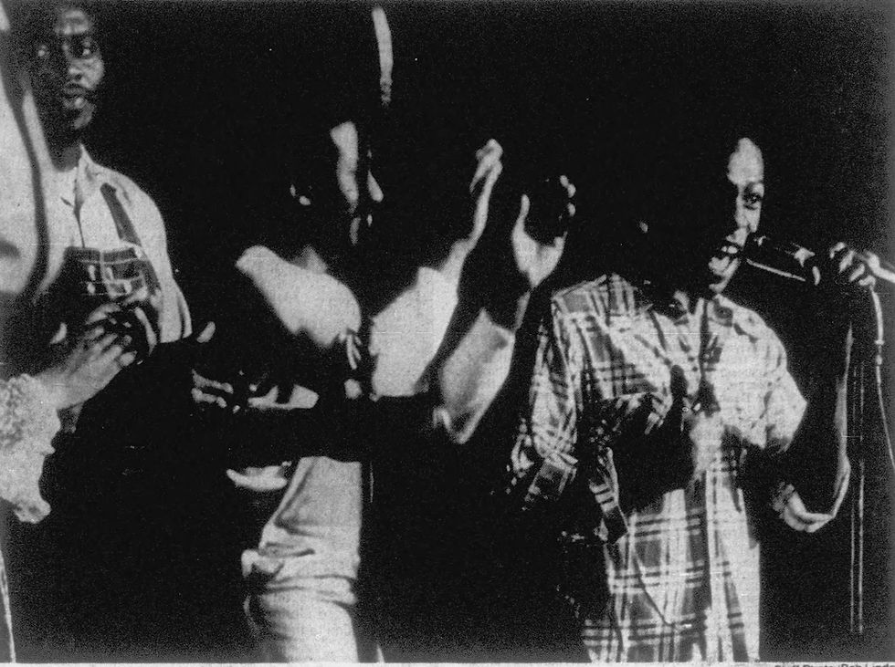 Singers from the Metropolitan Missionary Baptist Church performing on stage. Three men visible; one singing into microphone and another clapping.