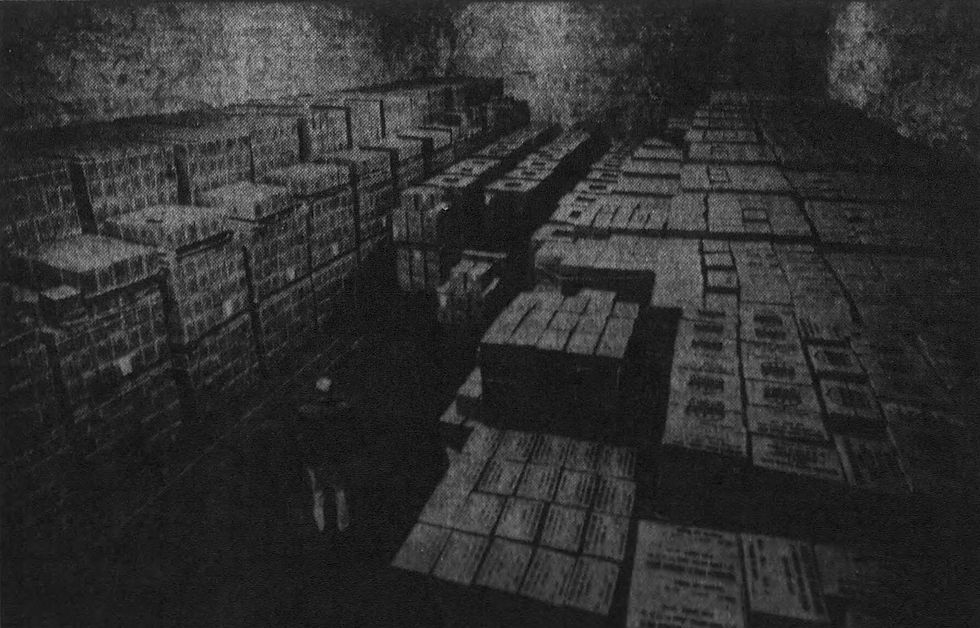 A photograph in newsprint of a man standing amid boxes. The details of the photograph are hard to make out.