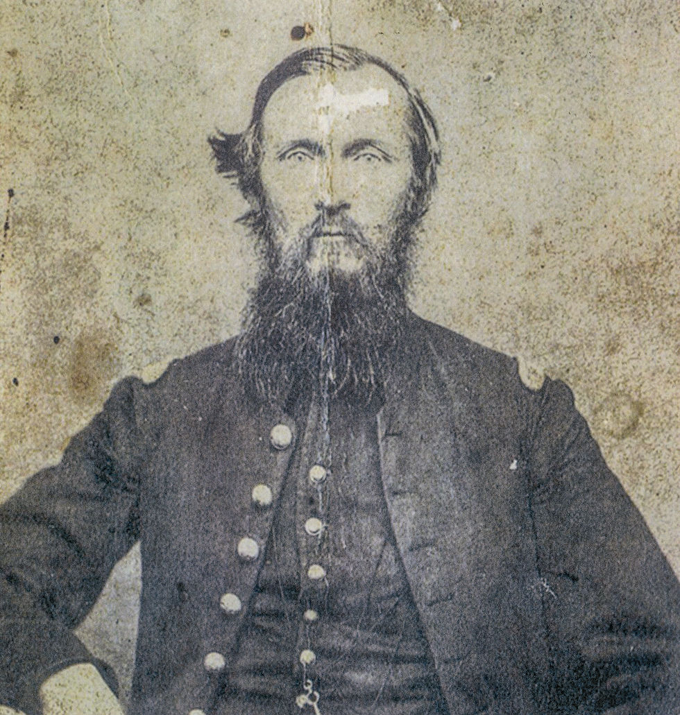 A portrait of Rowan E. M. Mack taken at some point in the early 1860s. The photograph is weather and creased down the middle. Mack is a white man and has a long, scraggly beard, middle length hair, and is in military uniform.