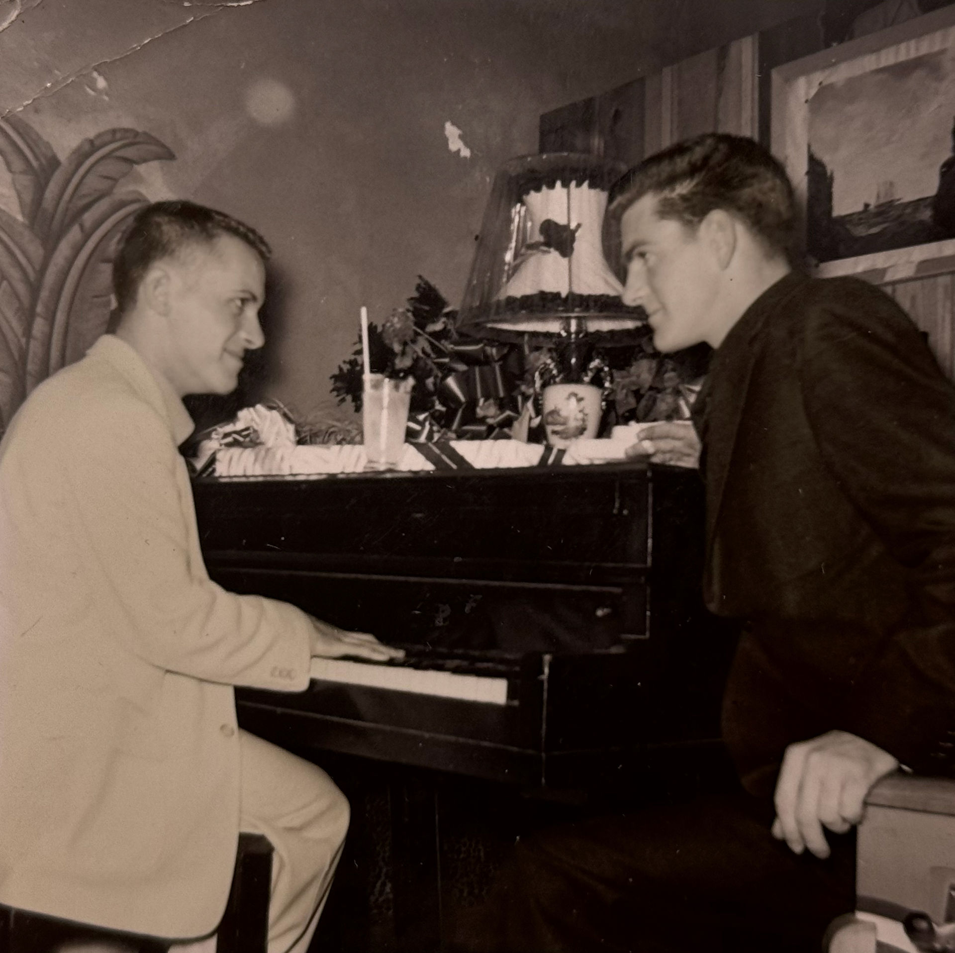 Two unidentified men gaze at one another at a piano.