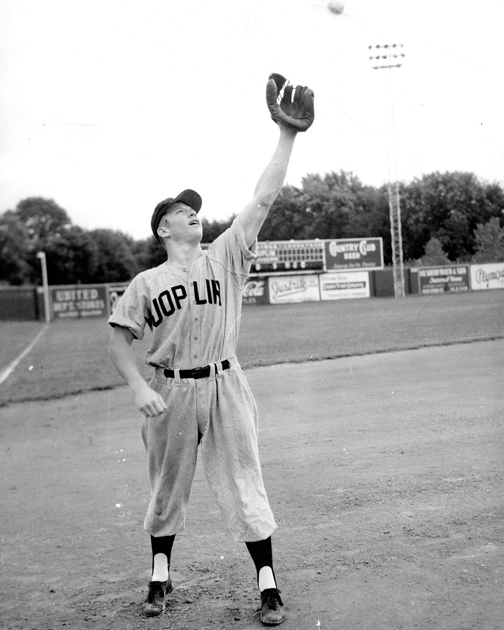 A black and white photograph of Mickey Mantle reaching to catch a baseball while playing for the Joplin Miners. Mantle's uniform reads "Joplin."