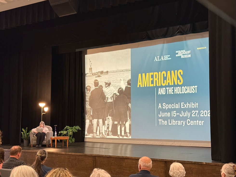 Erika Schwartz, an older woman, seated on the stage of Hatch Auditorium in front of an audience. Text on display reads: "Americans and the Holocaust: A Special Exhibit June 15-July 27, 2026 The Library Center."