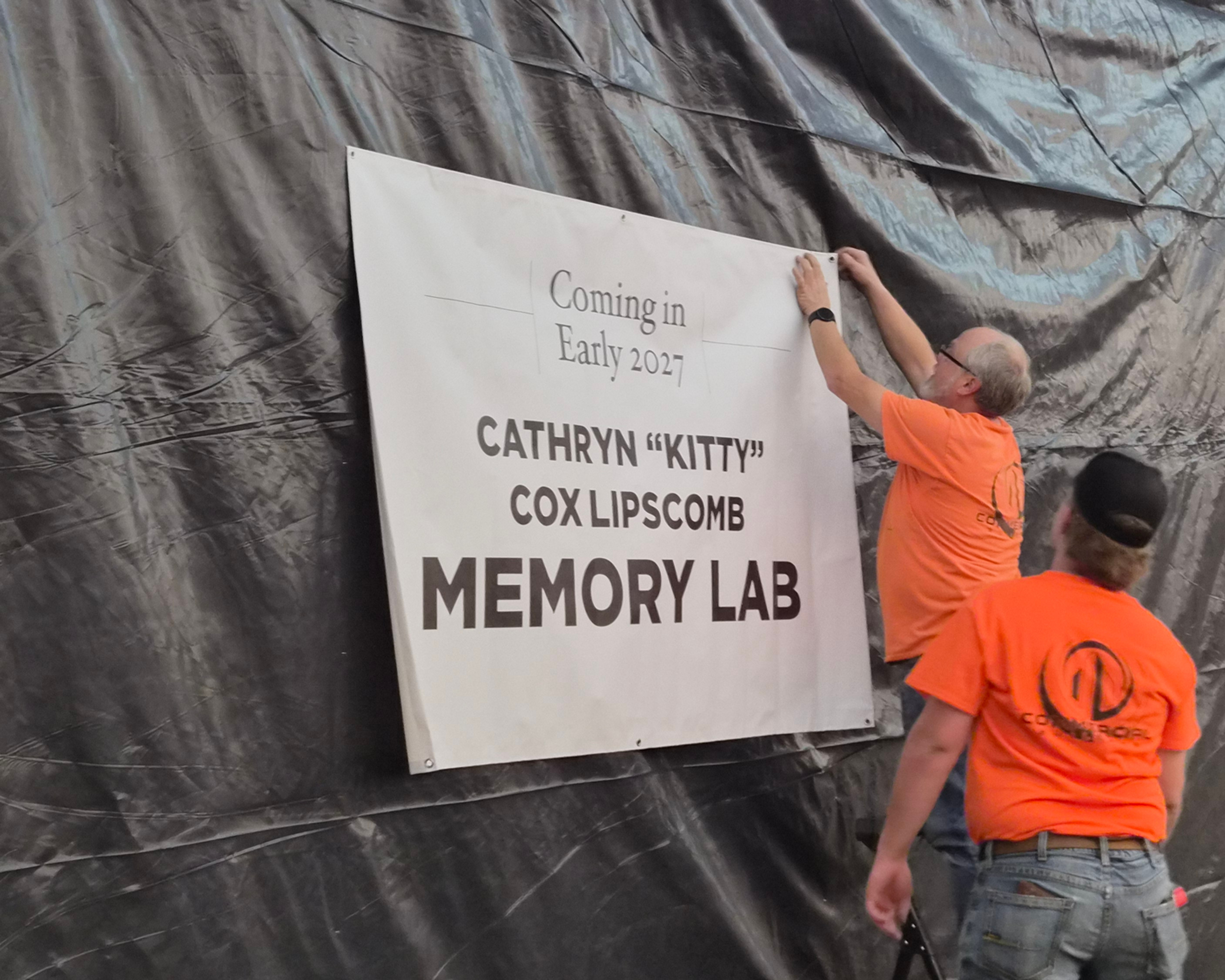 Workers put up a sign that reads "Coming in Early 2027: Cathryn 'Kitty' Cox Lipscomb Memory Lab."