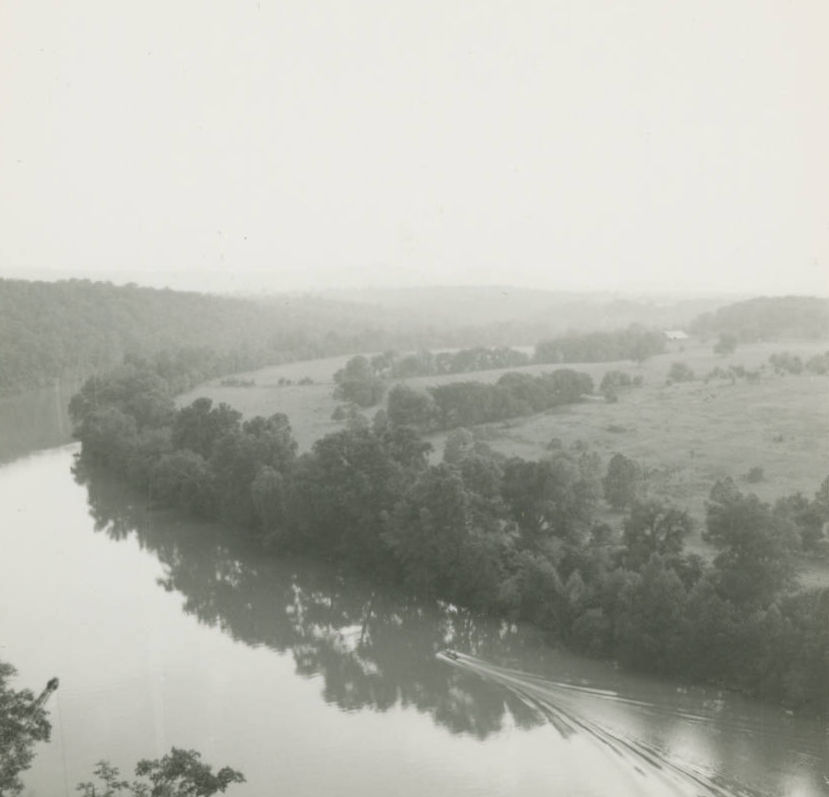 An overhead view of the White River from the construction site of the Table Rock Dam. A small boat moves downstream.