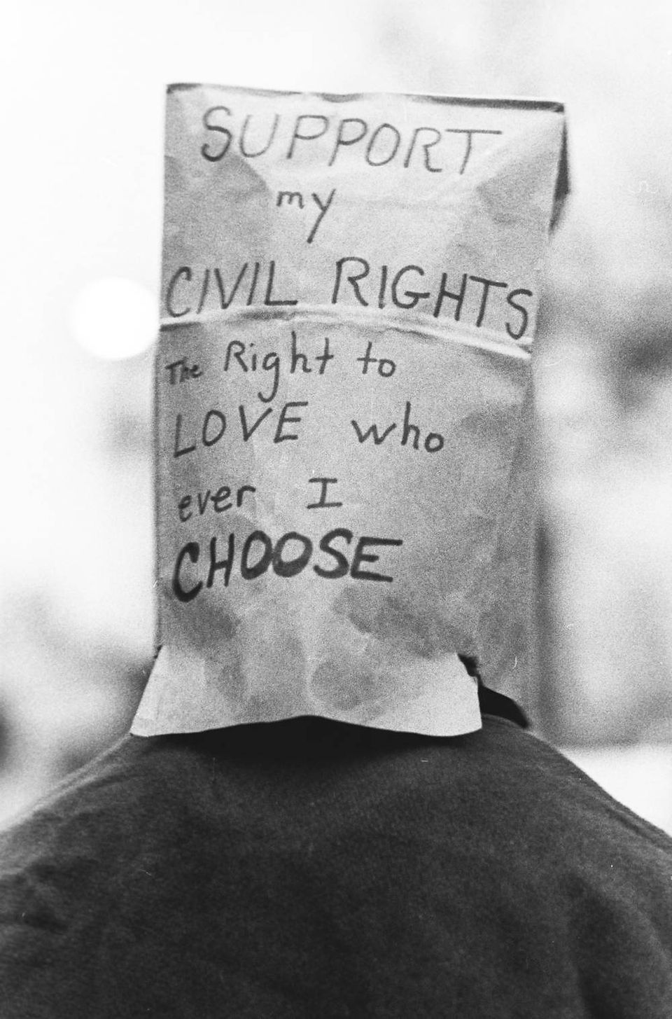 A woman marches with a bag over her head. Text on bag reads: "Support my Civil Rights. The right to LOVE who ever I choose."