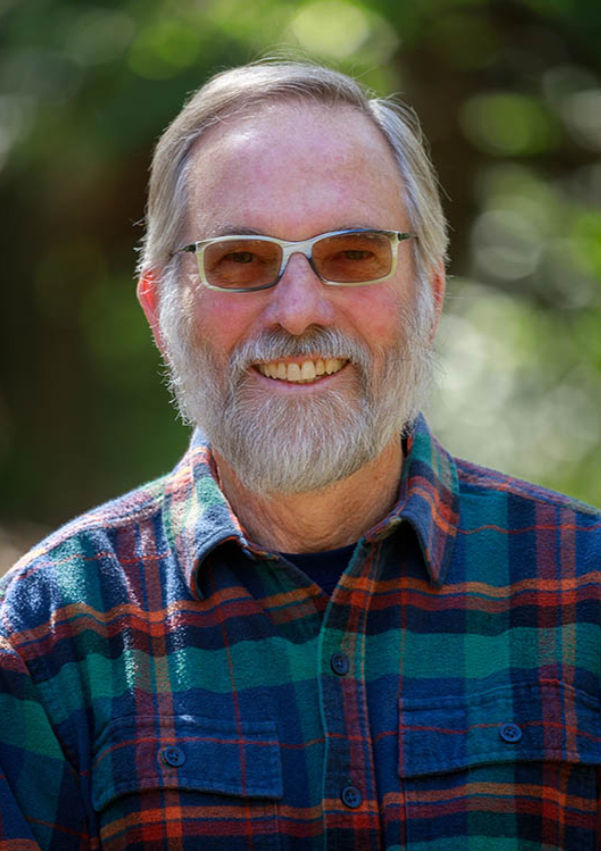 A portrait of Jim Mayfield. Mayfield is standing outdoors and is wearing sunglasses.