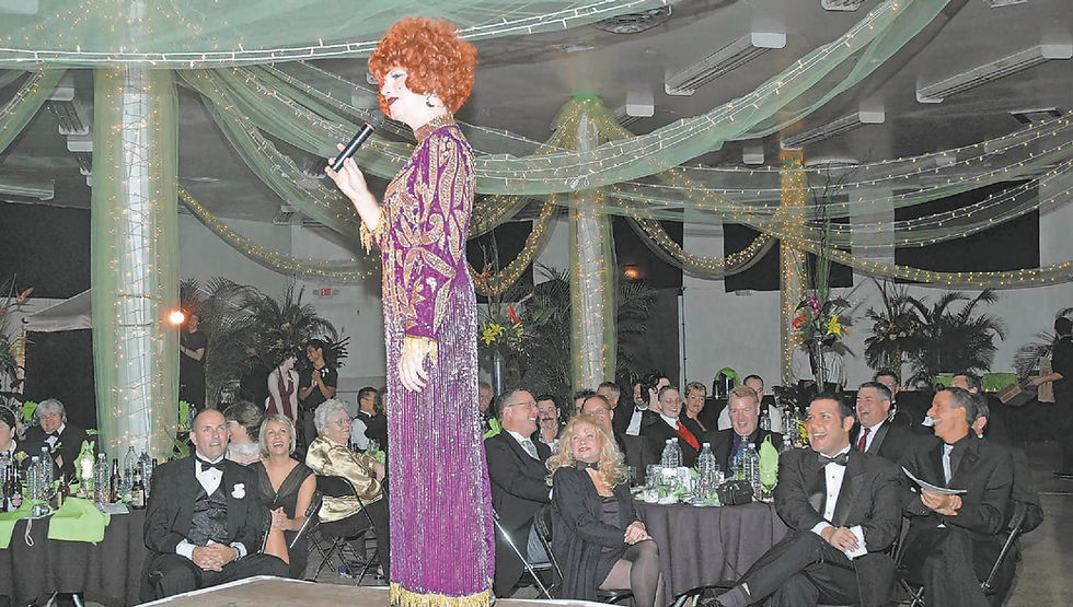 Miss Cleo, a drag queen wearing a curly red wig and a purple dress, stands on stage at the third annual Black Tie Affair in 2005.