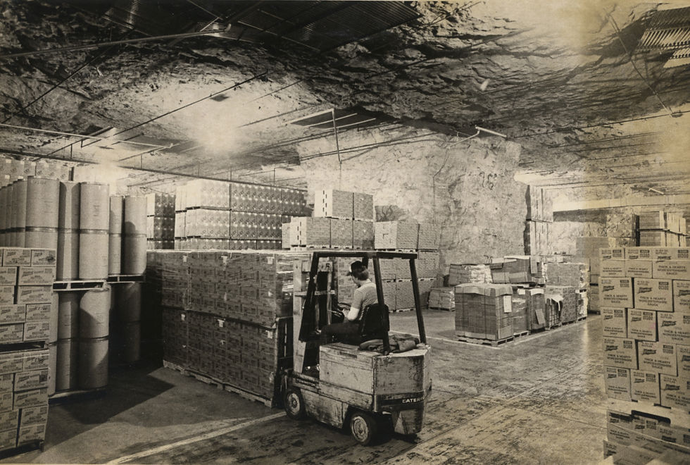 A man uses a forklift to move boxes of product in an underground storage space.