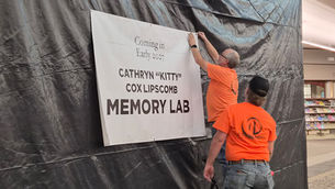 Workers put up a sign that reads "Coming in Early 2027: Cathryn 'Kitty' Cox Lipscomb Memory Lab."