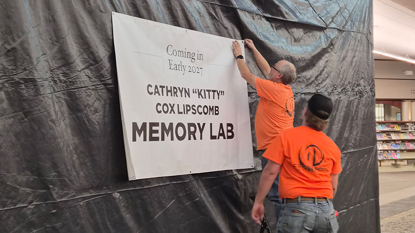 Workers put up a sign that reads "Coming in Early 2027: Cathryn 'Kitty' Cox Lipscomb Memory Lab."