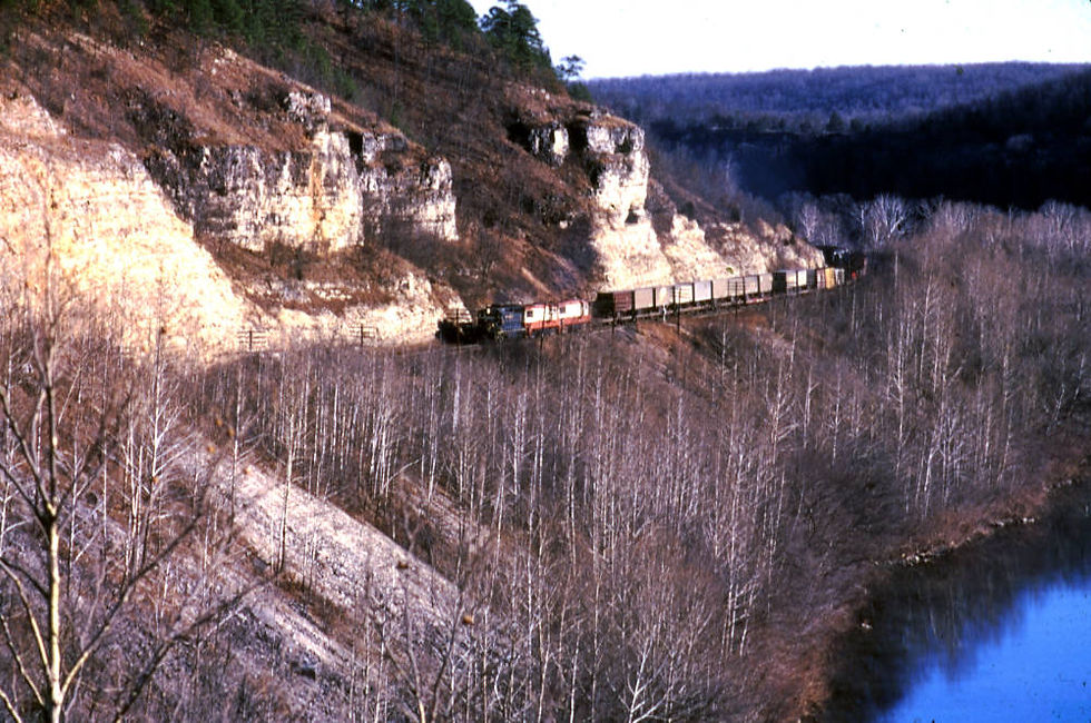A Frisco locomotive (EMD GP35 number 715) pulls a train along the bluffs of the Gasconade River. Bare trees cover the slope below the tracks.