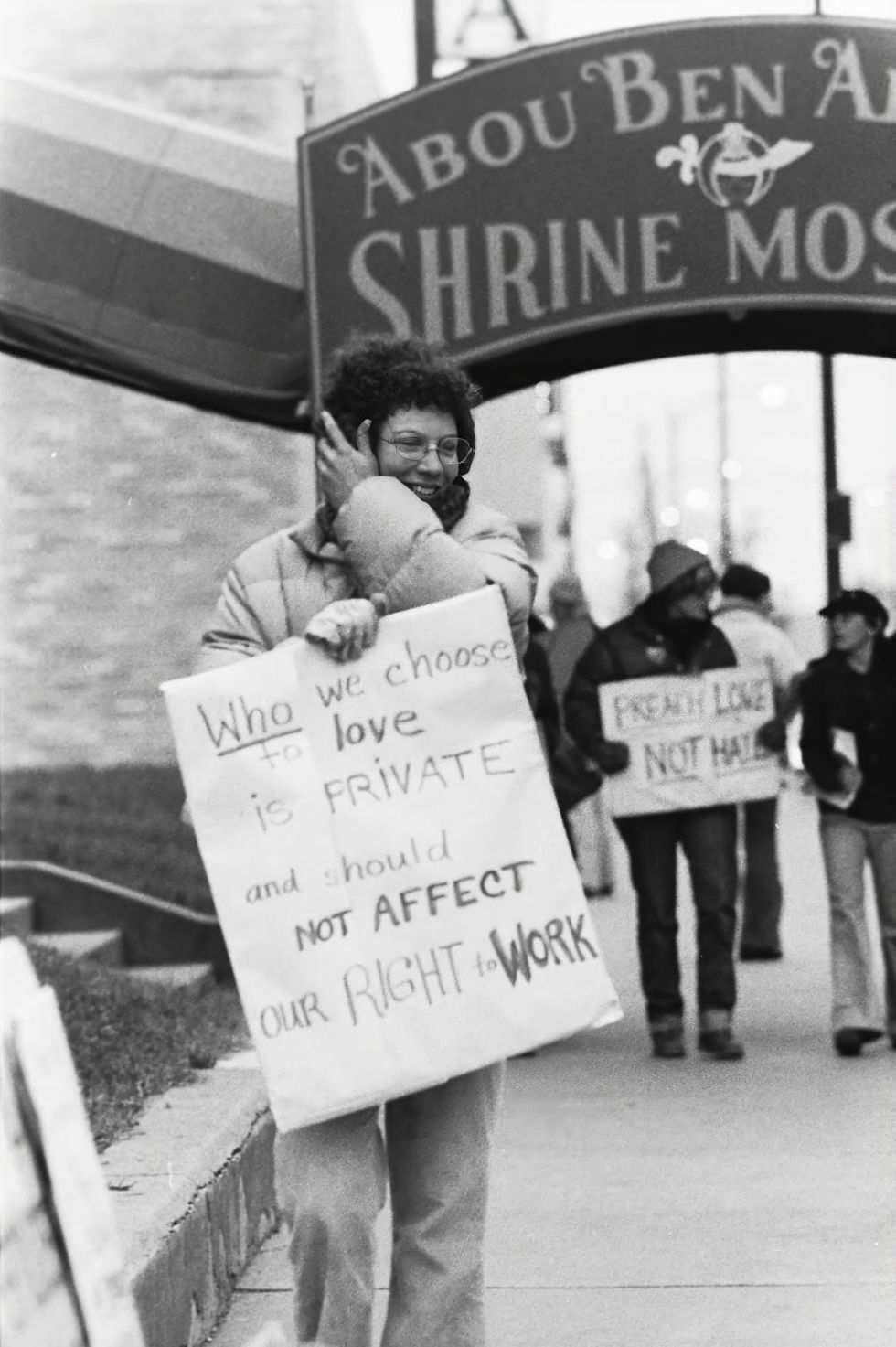 A protestor outside of an Anita Bryant event at Springfield's Shrine Mosque. Sign reads: "Who we choose to love is private and should not affect our right to work."