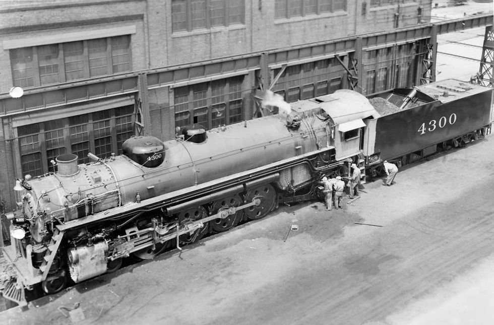 A black and white photograph of steam engine 4300 being worked on by Frisco staff at the Frisco West Shops. The photograph is shot from a wide overhead angle.