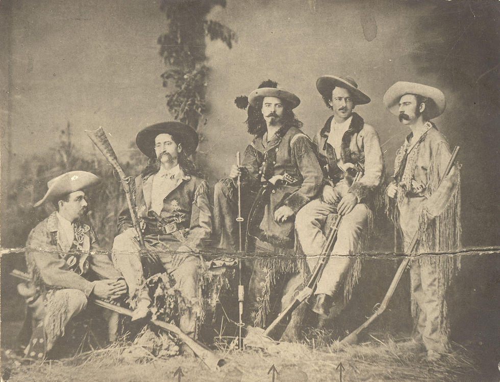 A sepia tone photo of five men in elaborate hats and costumes posing with large rifles. 