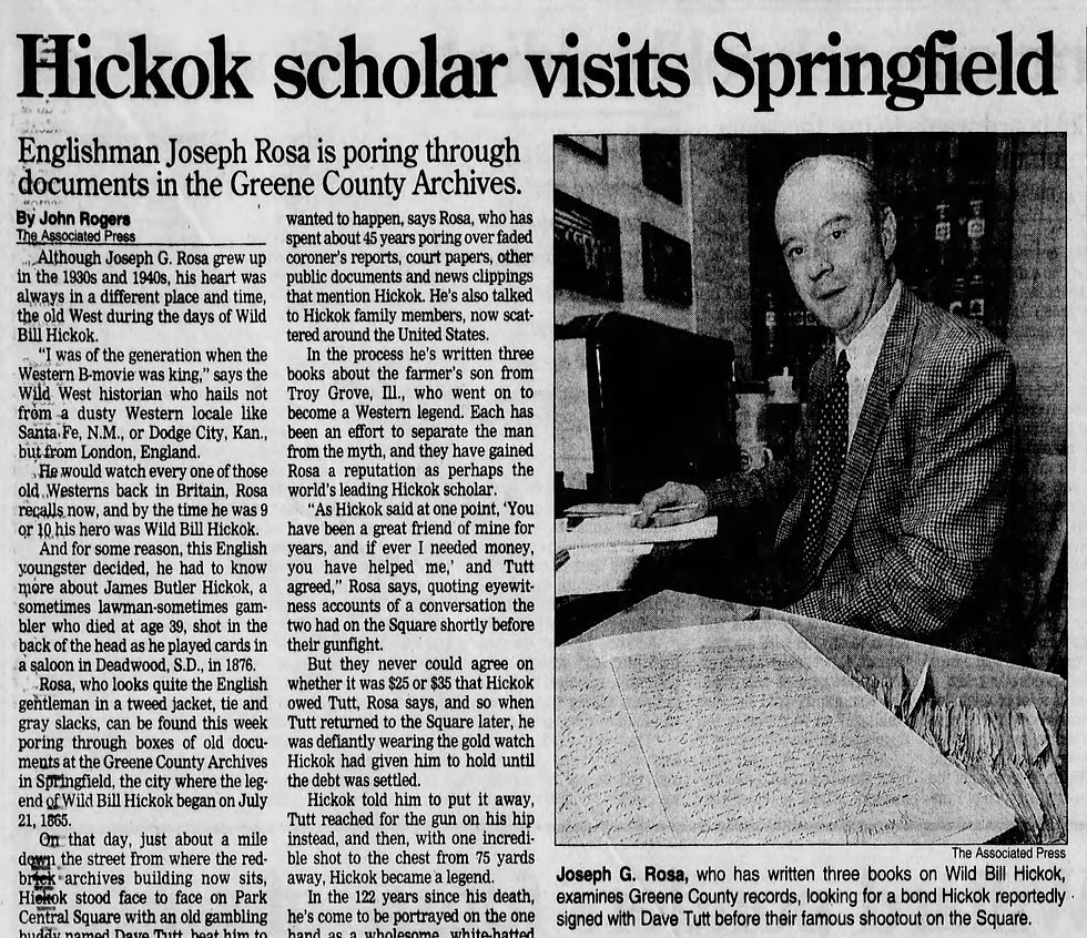 A newspaper clipping with the headline "Hickok scholar visits Springfield" with a photo of a man in a suit sitting near a box of files with a large handwritten document lying next to him. 