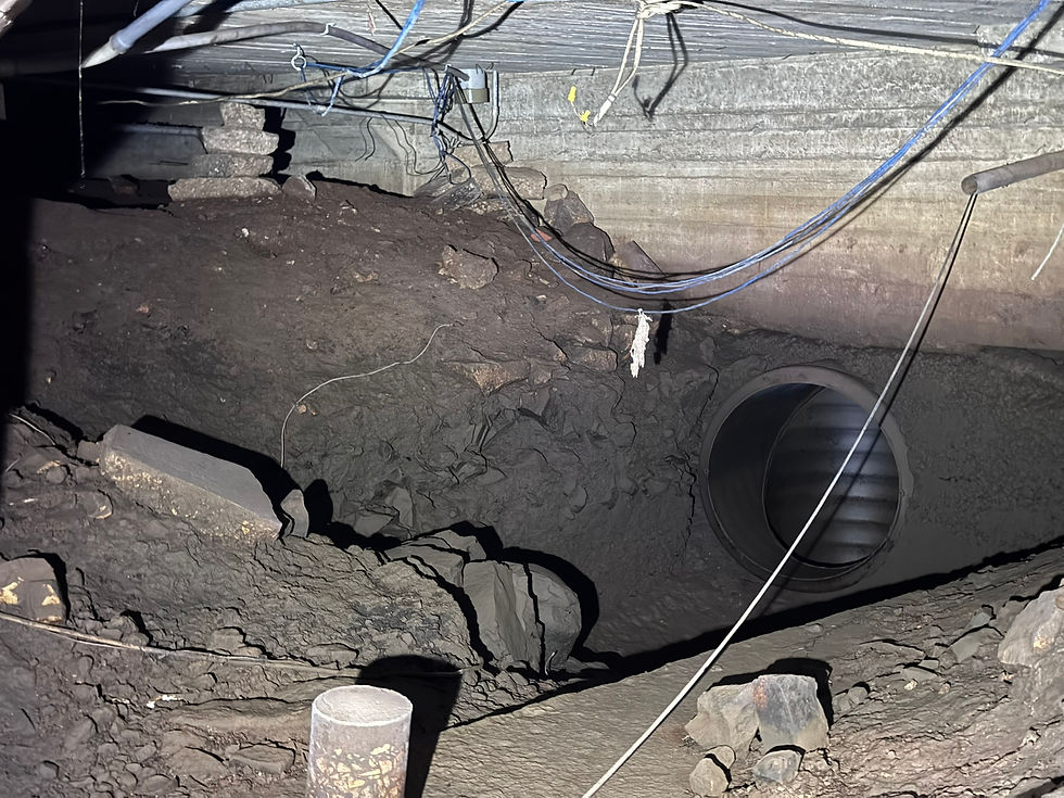 A courrogated metal culvert in a mud-covered wall in a basement