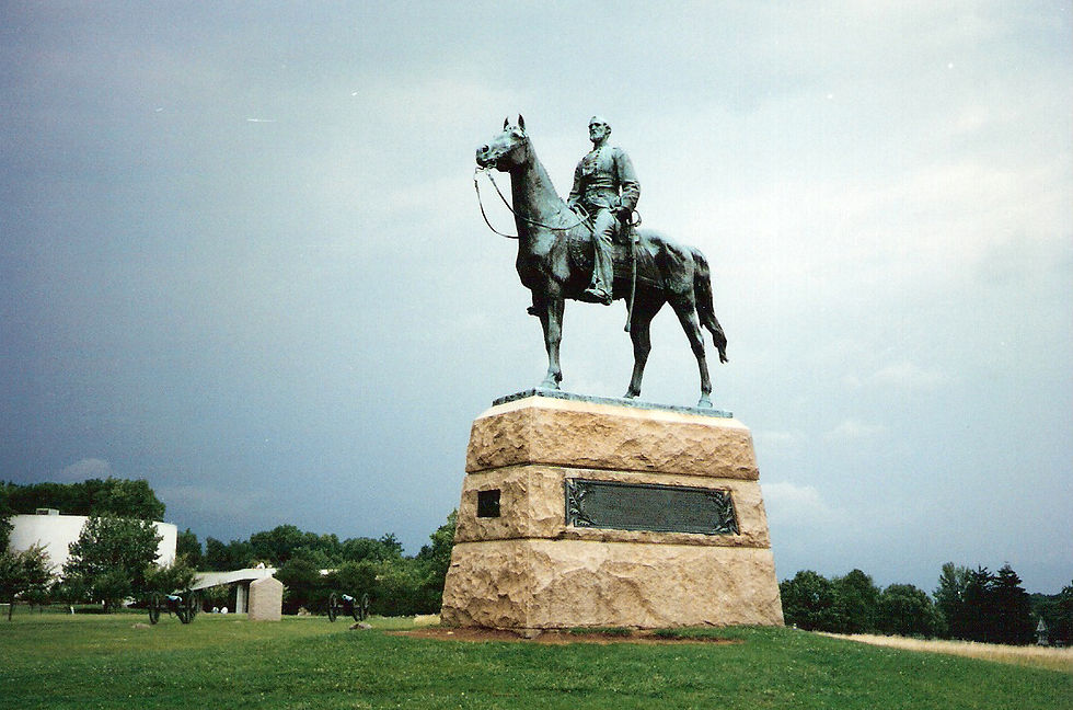 a color photograph shows a patina'ed statue of a man on a horse, mounted on a stone riser and standing in the middle of a grassy field littered with Civil War-era cannons