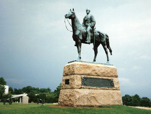 Mounted monument of a man on a horse standing in the middle of a grassy field