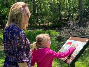 Child reading a StoryWalk while on a trail