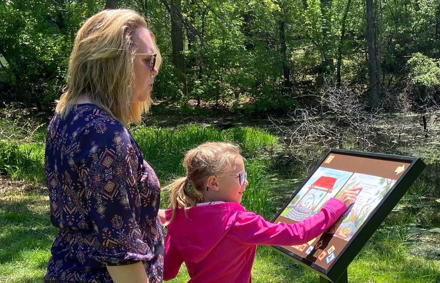 Child reading a StoryWalk while on a trail